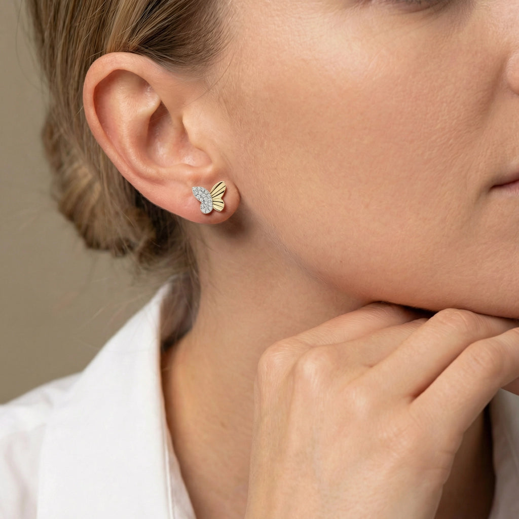 A pair of delicate butterfly-shaped diamond stud earrings in two-tone 14K gold on ear.