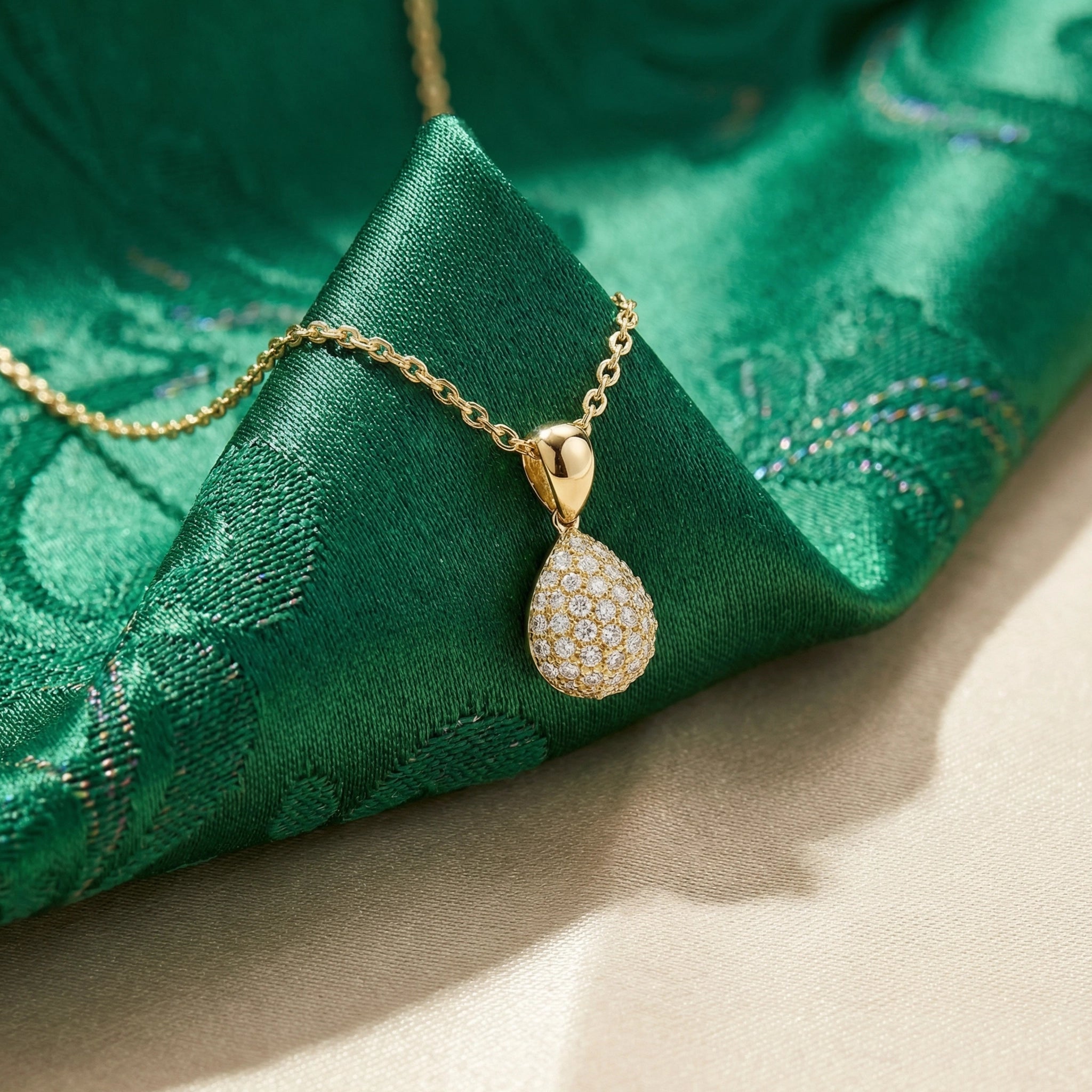 Gold teardrop pendant necklace on a green fabric background