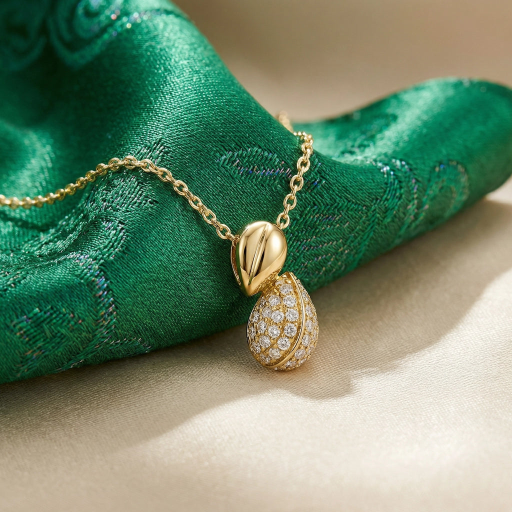 Gold necklace with a leaf and teardrop pendant on green fabric