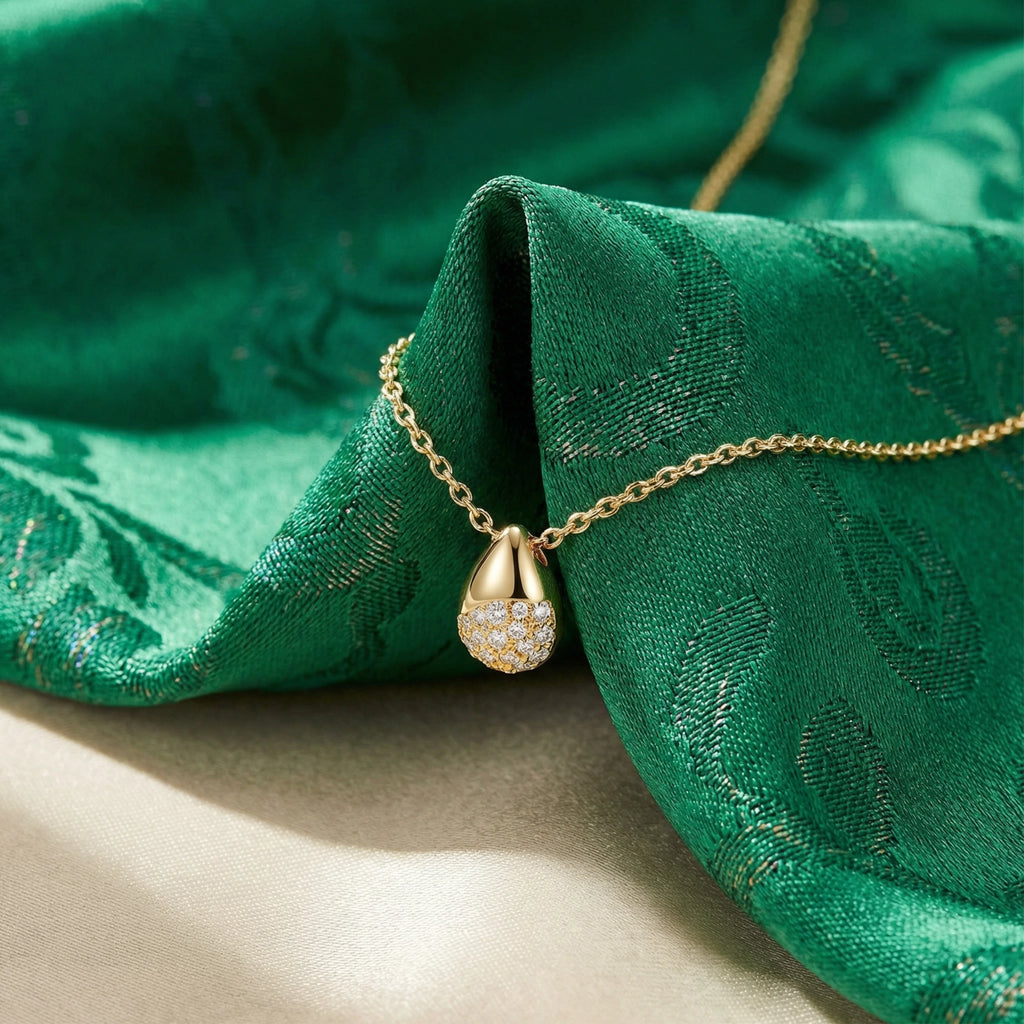 Gold necklace with a teardrop pendant on green fabric
