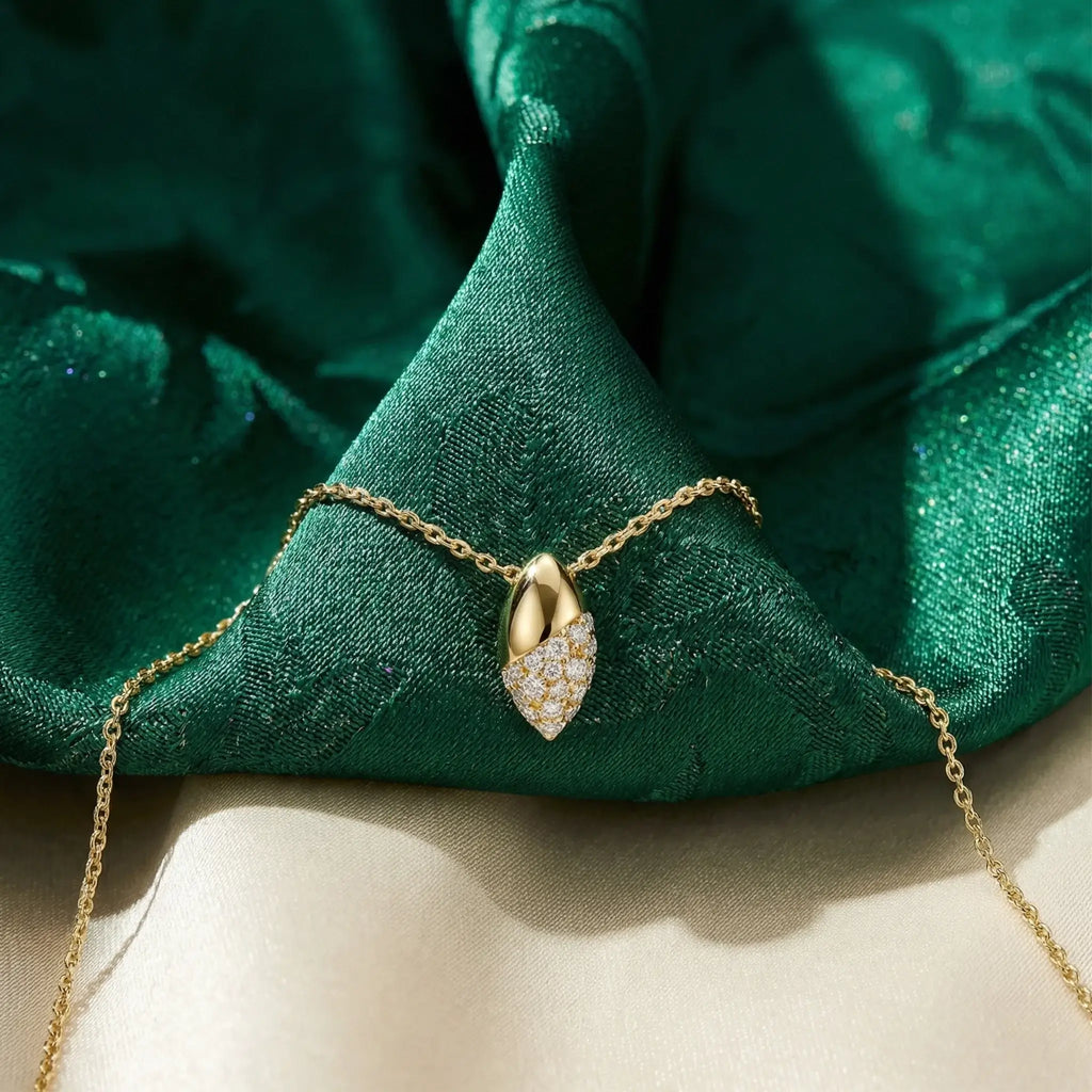 Gold necklace with a olive-shaped pendant on green fabric