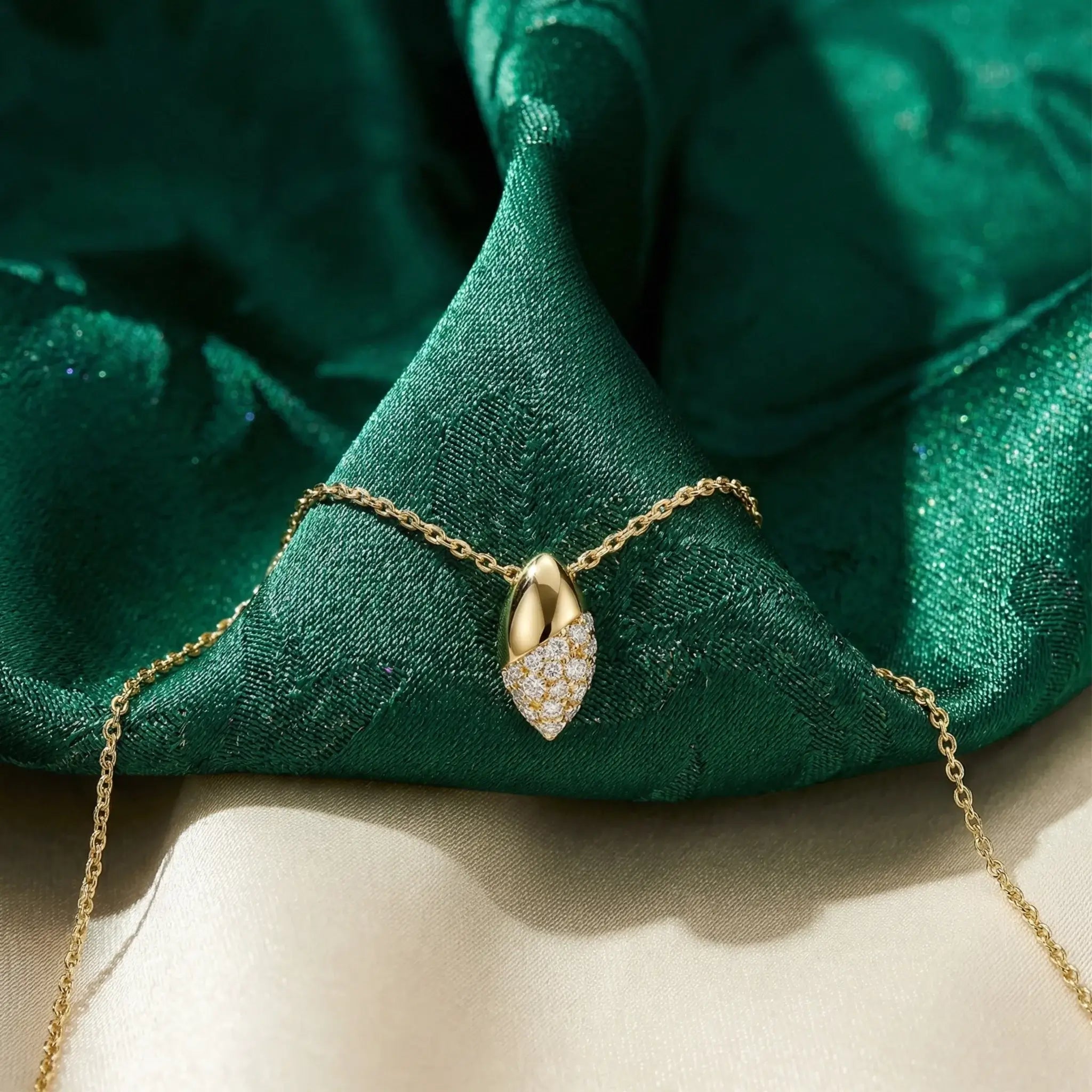 Gold necklace with a olive-shaped pendant on green fabric