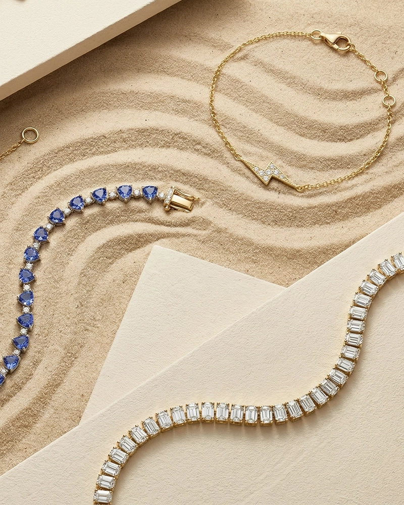 A curated flat lay of BeBling bracelets including a diamond line tennis bracelet, a paperclip chain, and a delicate charm bracelet, ready for stacking.