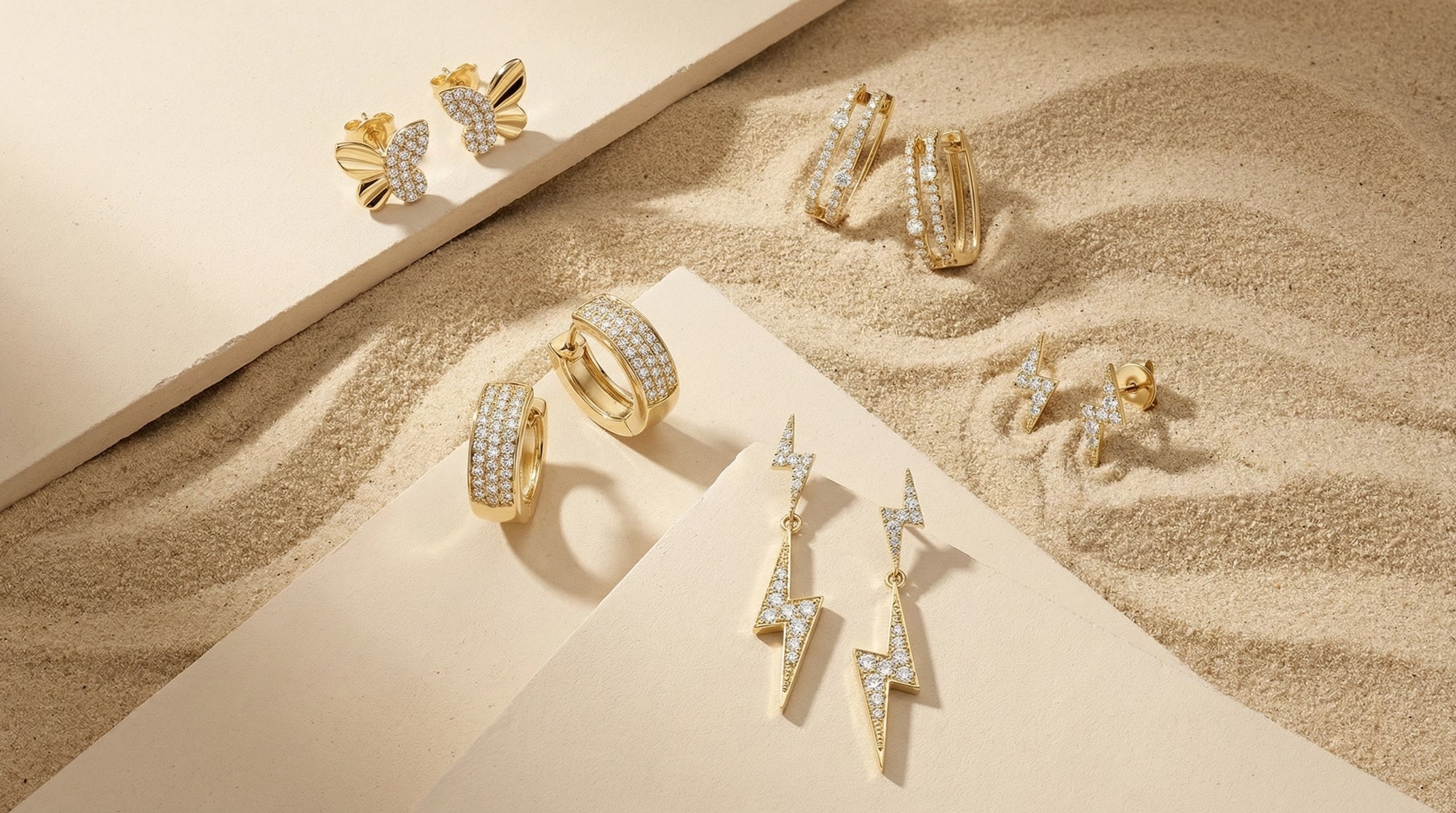 A curated assortment of BeBling earrings displayed on a velvet tray, featuring diamond studs, huggie hoops, and chandelier drop earrings in mixed metals.