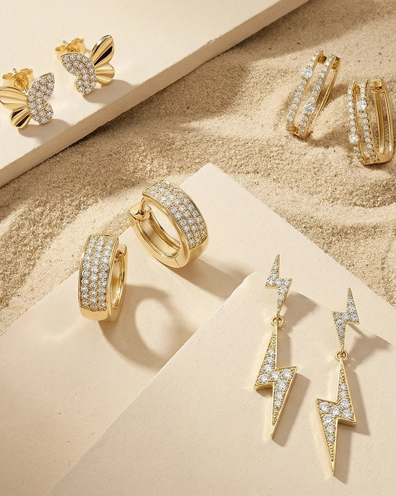 A curated assortment of BeBling earrings displayed on a velvet tray, featuring diamond studs, huggie hoops, and chandelier drop earrings in mixed metals.